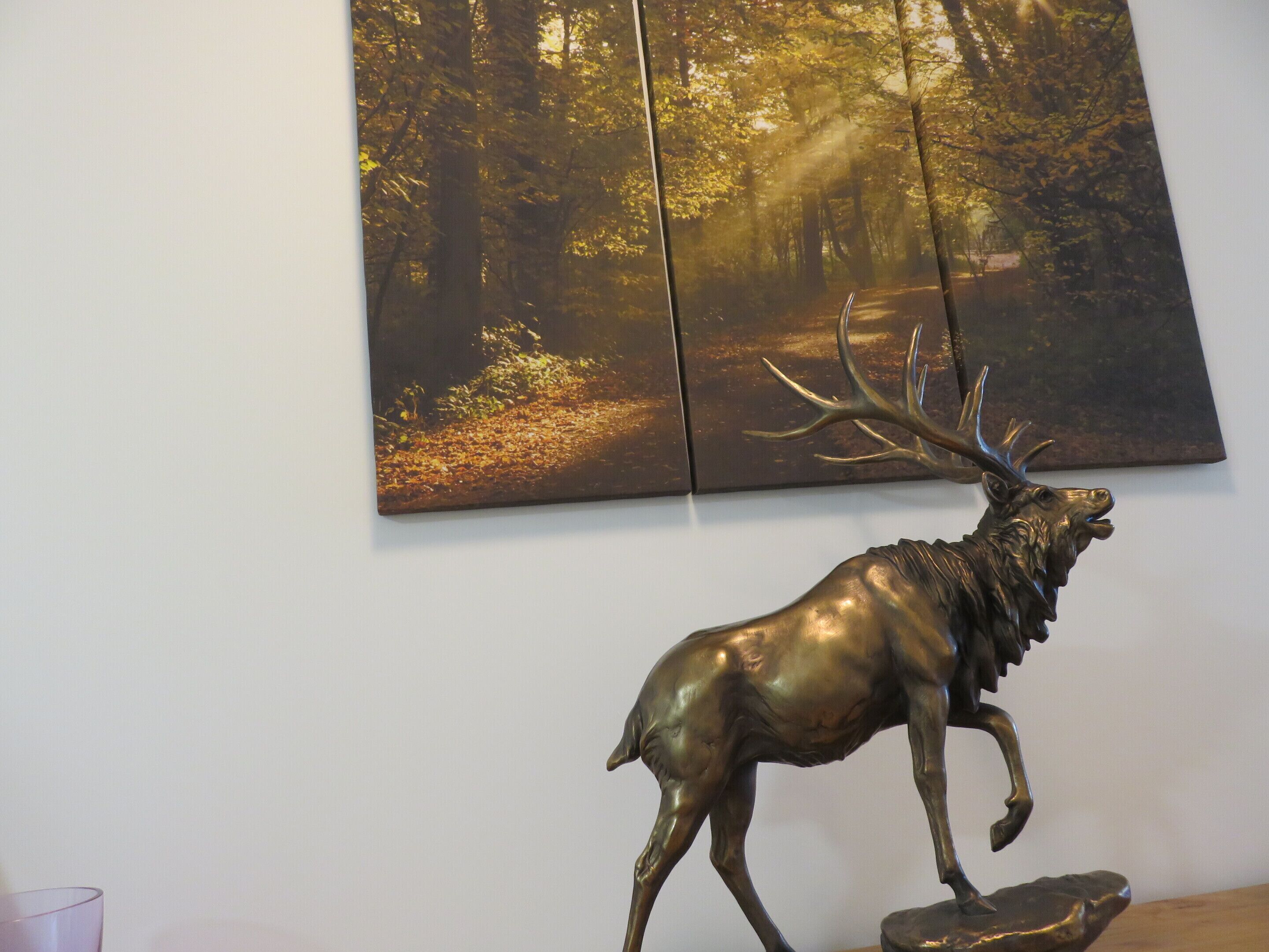 A room with a large painting of a forest and a bronze deer sculpture.