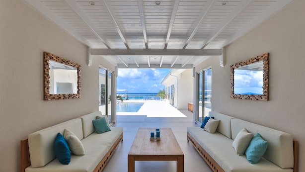 Un intérieur moderne avec deux canapés placés face à une grande fenêtre donnant sur une piscine et l’océan.