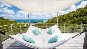 Un hamac avec des coussins, installé sur un balcon offrant une vue panoramique sur l’océan et la végétation.