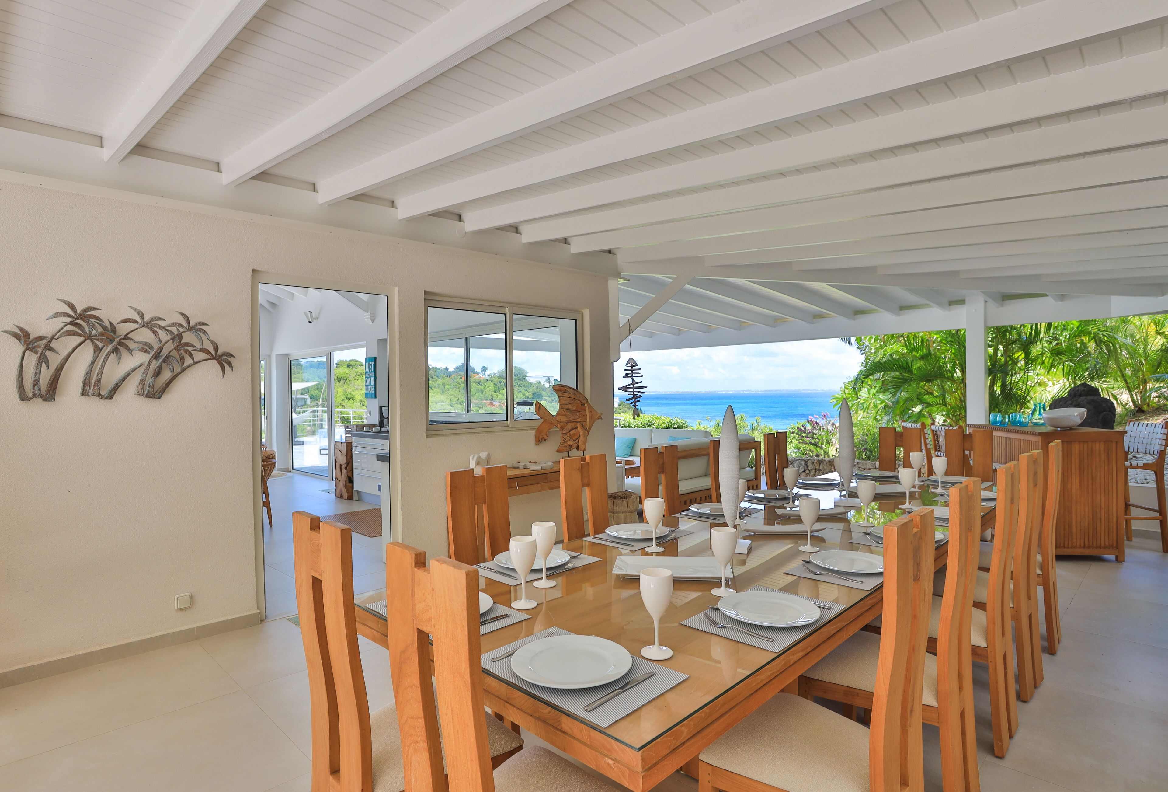 A dining area with a glass table, wooden chairs, and a view of the ocean.