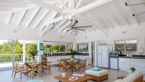 Un vaste espace de vie doté d’un haut plafond, comprenant une table à manger, des canapés et un coin cuisine avec vue sur l’extérieur.