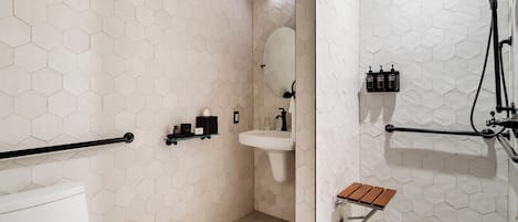 A bathroom with a hexagonal tile pattern, a white sink, a mirror, a handheld showerhead, and a wooden bench.