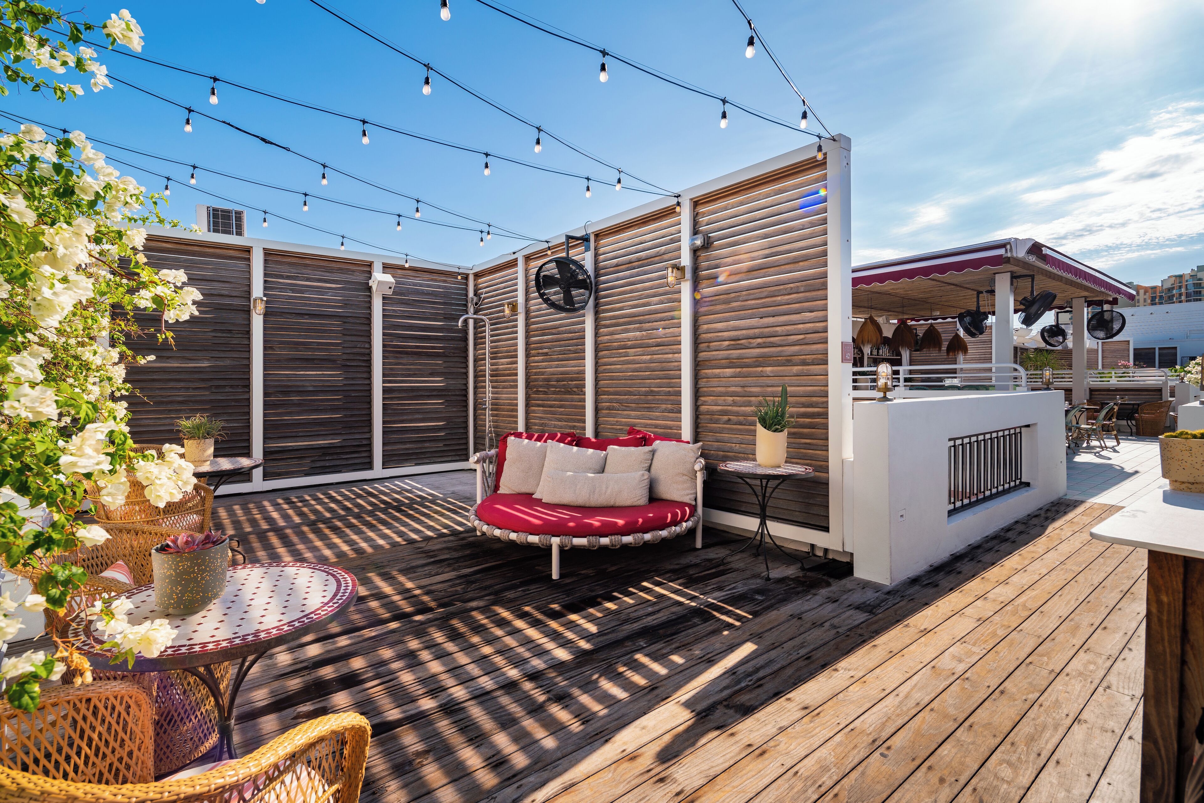 A wooden deck with a red cushioned seating area, wicker chairs, and string lights.