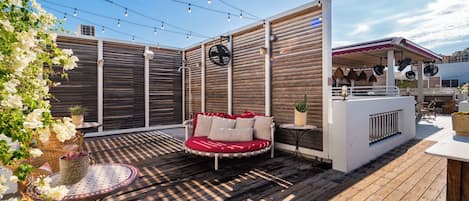 A wooden deck with a red cushioned seating area, wicker chairs, and string lights.