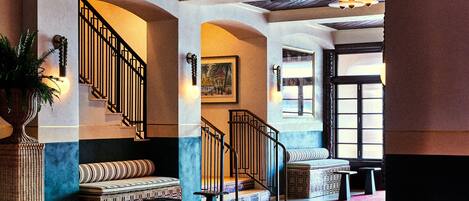 A grand lobby with a staircase, seating areas, and a large window.