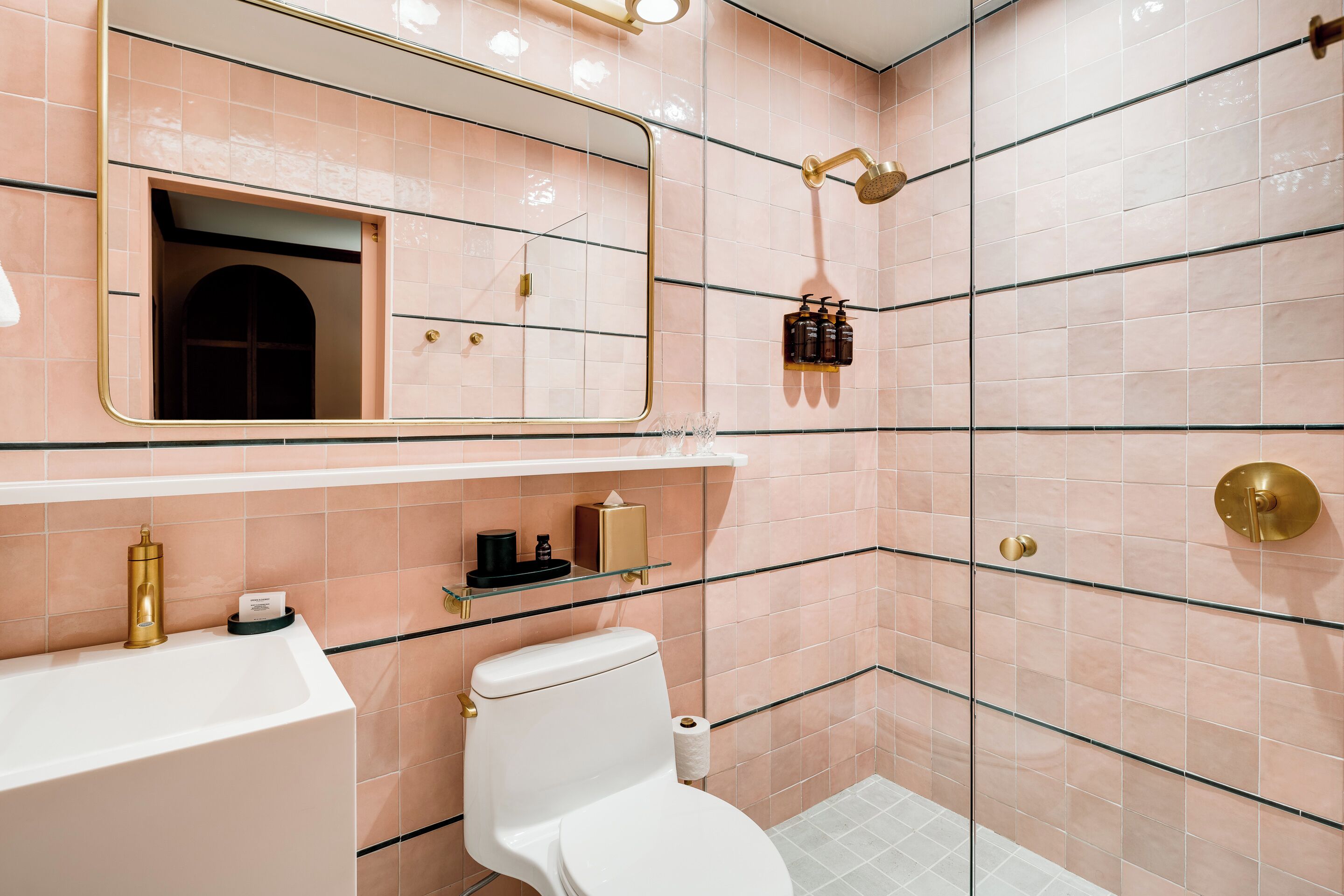 Un bagno con un lavandino bianco, un water, uno specchio e una doccia con soffione dorato.