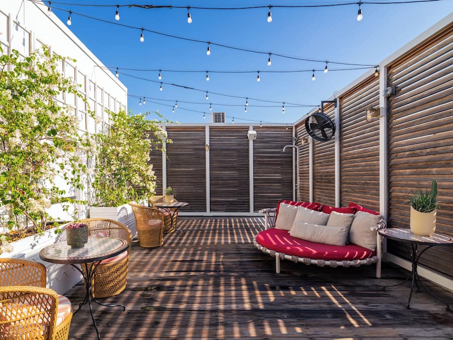 An outdoor patio with wicker furniture, a red cushioned sofa, and string lights.