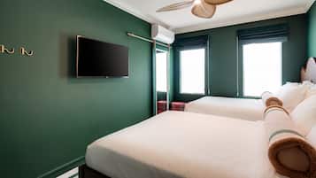 A hotel room with two beds, a flat-screen TV, an air conditioning unit, and a ceiling fan.