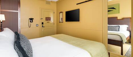 A hotel room with a bed, a ceiling fan, a flat-screen TV, a telephone, and a mirror.