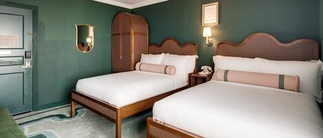 A hotel room with two wooden beds, a green accent wall, a ceiling fan, and a green accent chair.