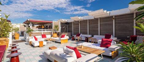 An outdoor seating area with multiple sofas and tables, a covered section with a red and white awning, and a view of the sky.