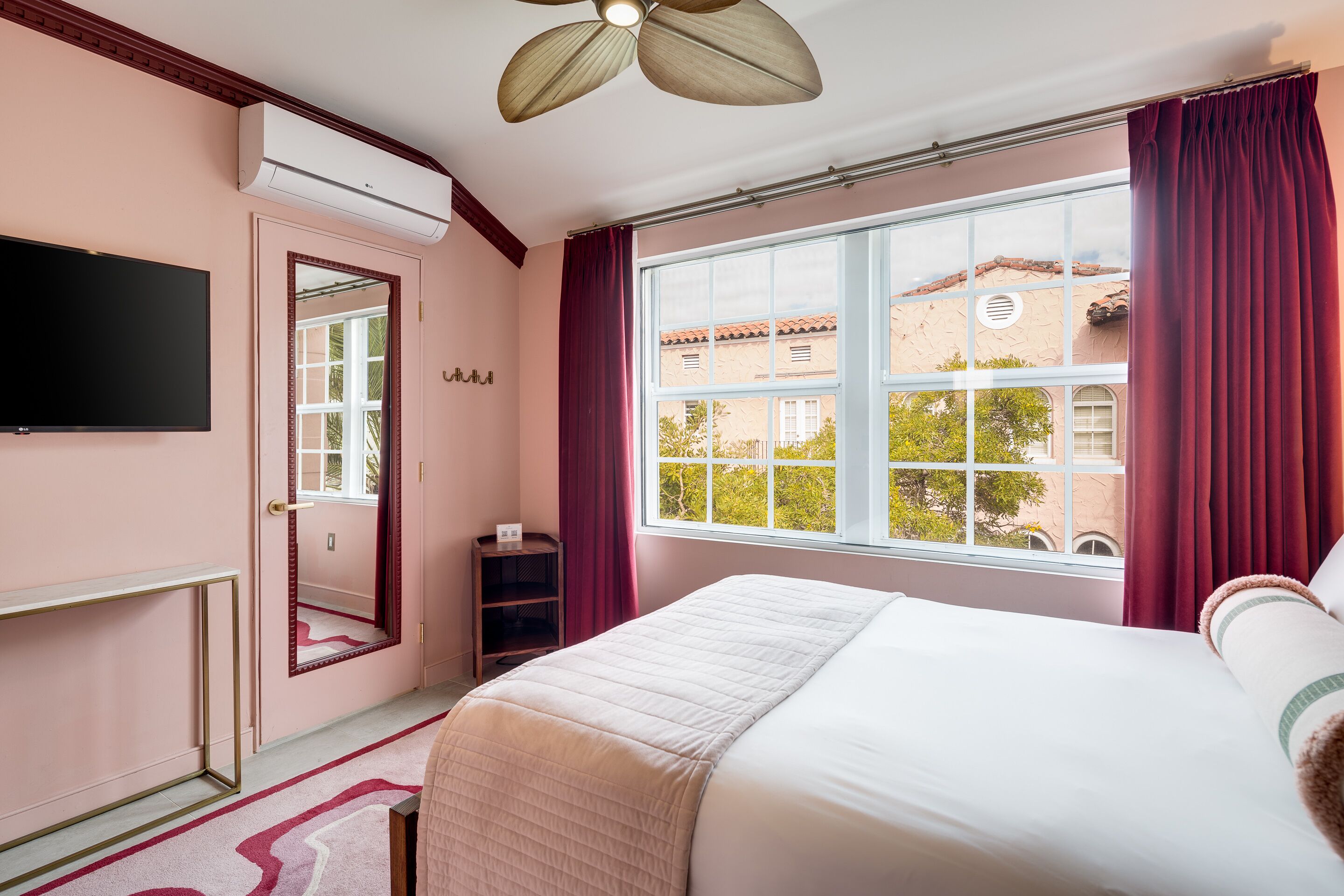 Une chambre à coucher comprenant un lit, une télévision, une fenêtre avec des rideaux, un miroir et un appareil de climatisation.