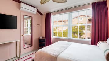Une chambre à coucher comprenant un lit, une télévision, une fenêtre avec des rideaux, un miroir et un appareil de climatisation.