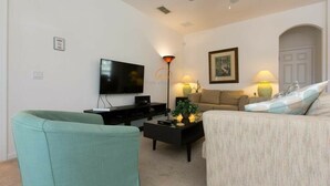 Ein Wohnzimmer mit Flachbildfernseher, Deckenventilator, Sofa, Couchtisch und zwei Lampen.