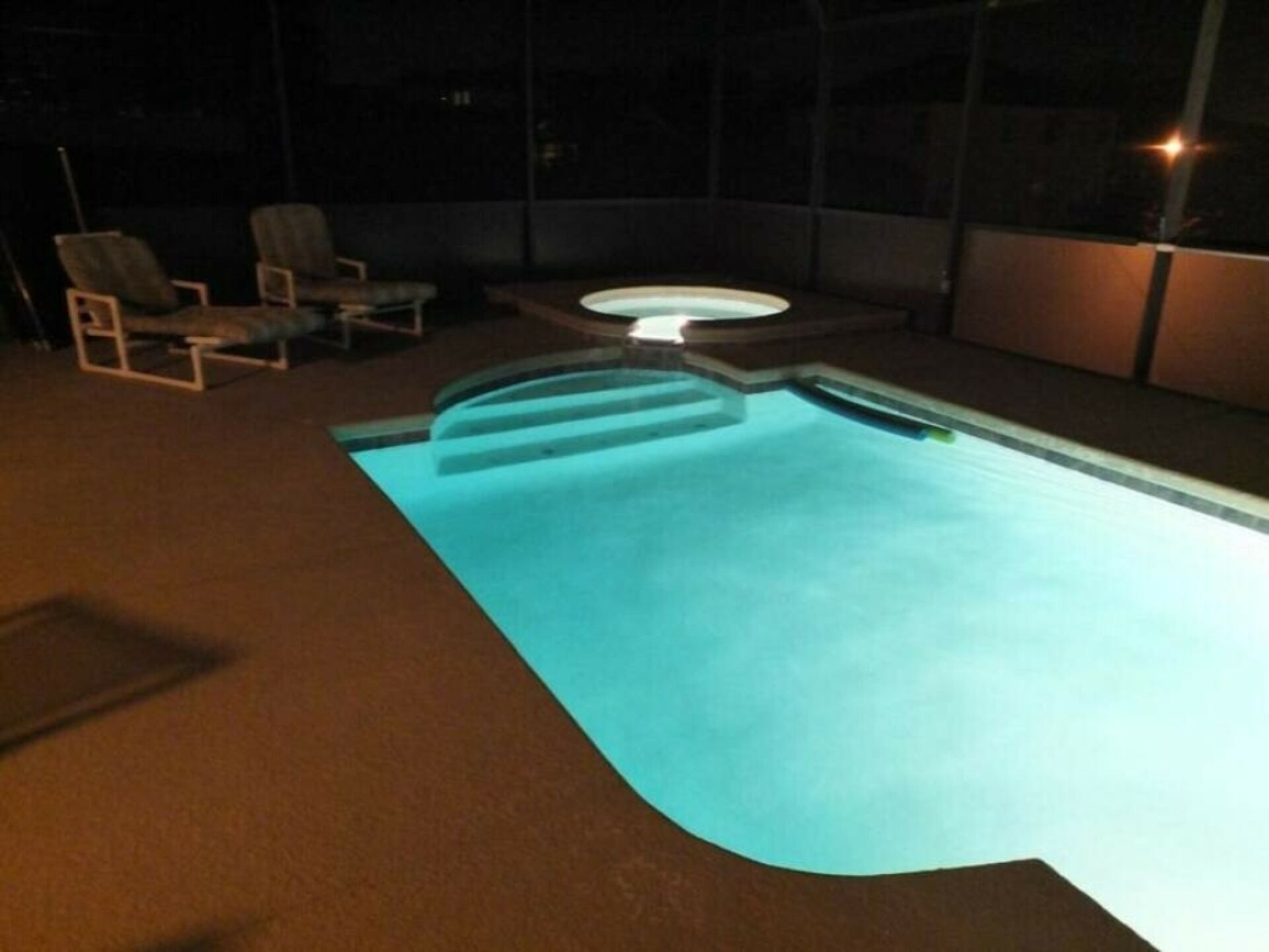 Piscina externa com hidromassagem, rodeada por cadeiras e um espaço coberto.