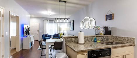 A modern kitchen with granite countertops, a dishwasher, and a dining area with a TV.