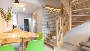 A modern interior with a wooden staircase, a dining area with green chairs, and a stone wall. - Apartamenty Domki Giewont (Zakopane)