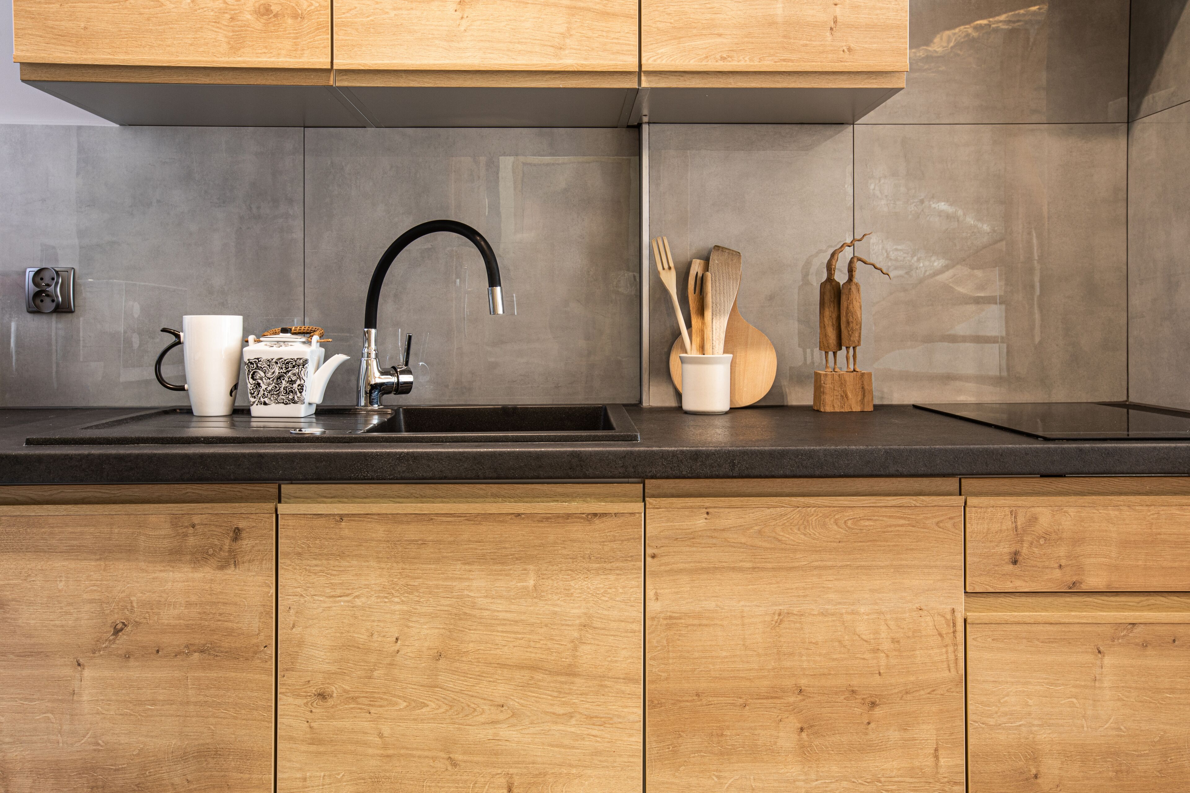Una cucina moderna con mobili in legno, un piano di lavoro nero, un lavello in acciaio inossidabile e un servizio da tè.