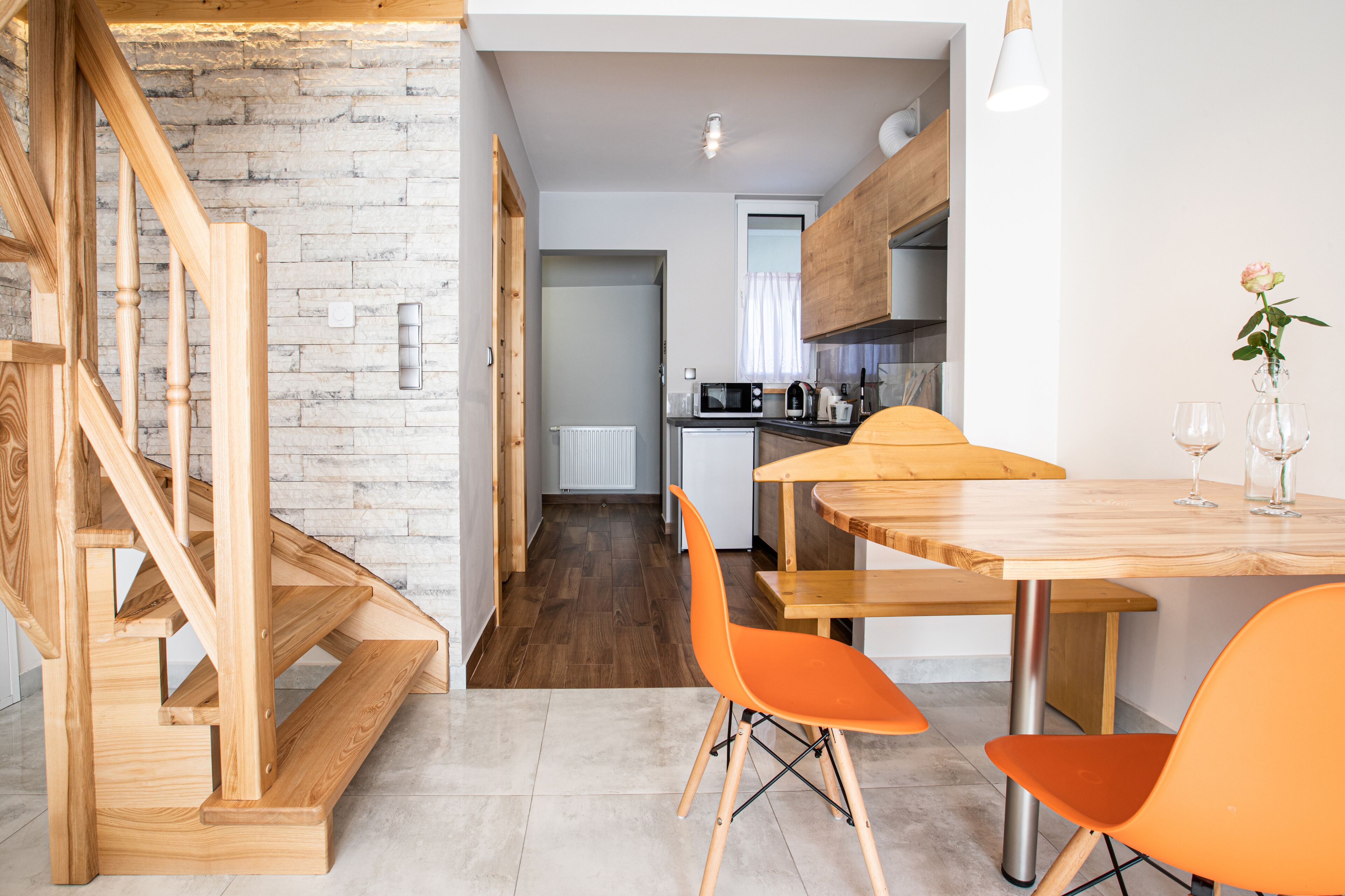 A modern kitchen with wooden cabinets, a dining table with orange chairs, and a staircase with wooden steps.