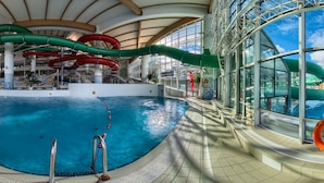 An indoor swimming pool with multiple water slides, a glass-enclosed area, and a view of the sky. - Apartamenty Domki Giewont (Zakopane)