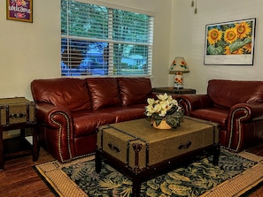 A living room with a brown leather sofa, a vintage suitcase, and a floral arrangement on a table.