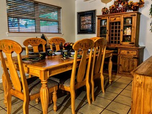 Un comedor con una mesa y sillas de madera, un aparador con puertas de cristal y una ventana con persianas.