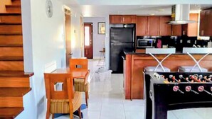 Una cocina moderna con una isla central, una escalera de madera y un comedor con mesa de futbolín.