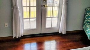 Una habitación con un amplio ventanal corredera que da a un balcón, suelo de madera y una cama con cubrecama blanca.