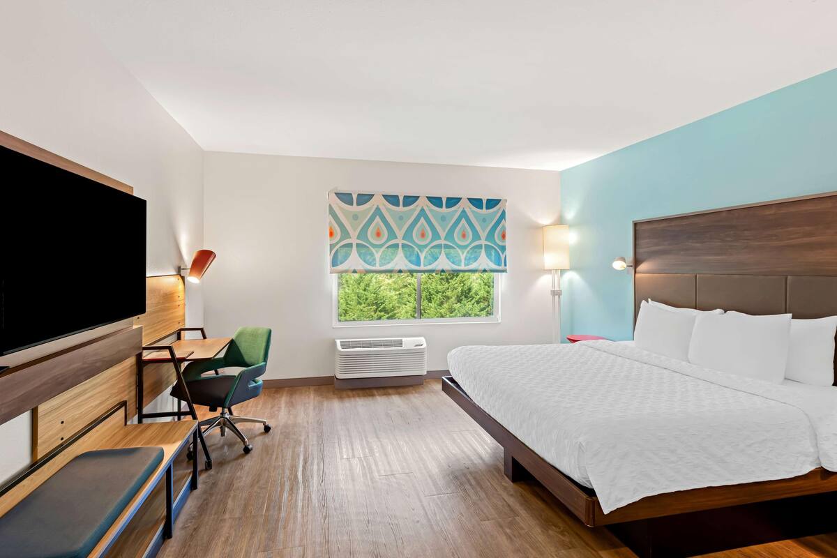 Ein Hotelzimmer mit einem Bett, einem Schreibtisch mit Stuhl, einem Fernseher, einem Fenster mit Blick und einer Wandklimaanlage.