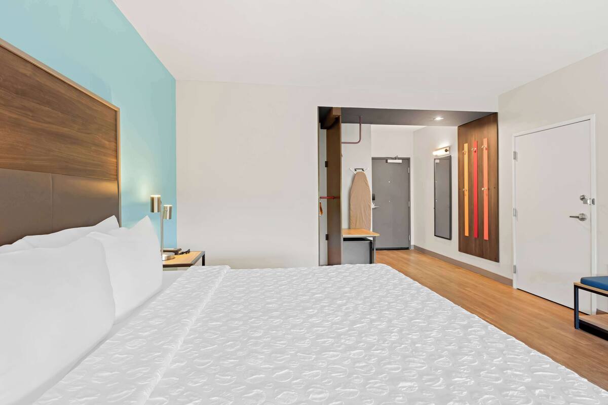 Ein modernes Hotelzimmer mit einem großen Bett, einem Holz-Kopfteil, einem Nachttisch und einer Wandlampe.
