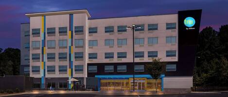 A modern hotel with a multi-story structure, a prominent entrance with glass doors, and a parking lot in front.