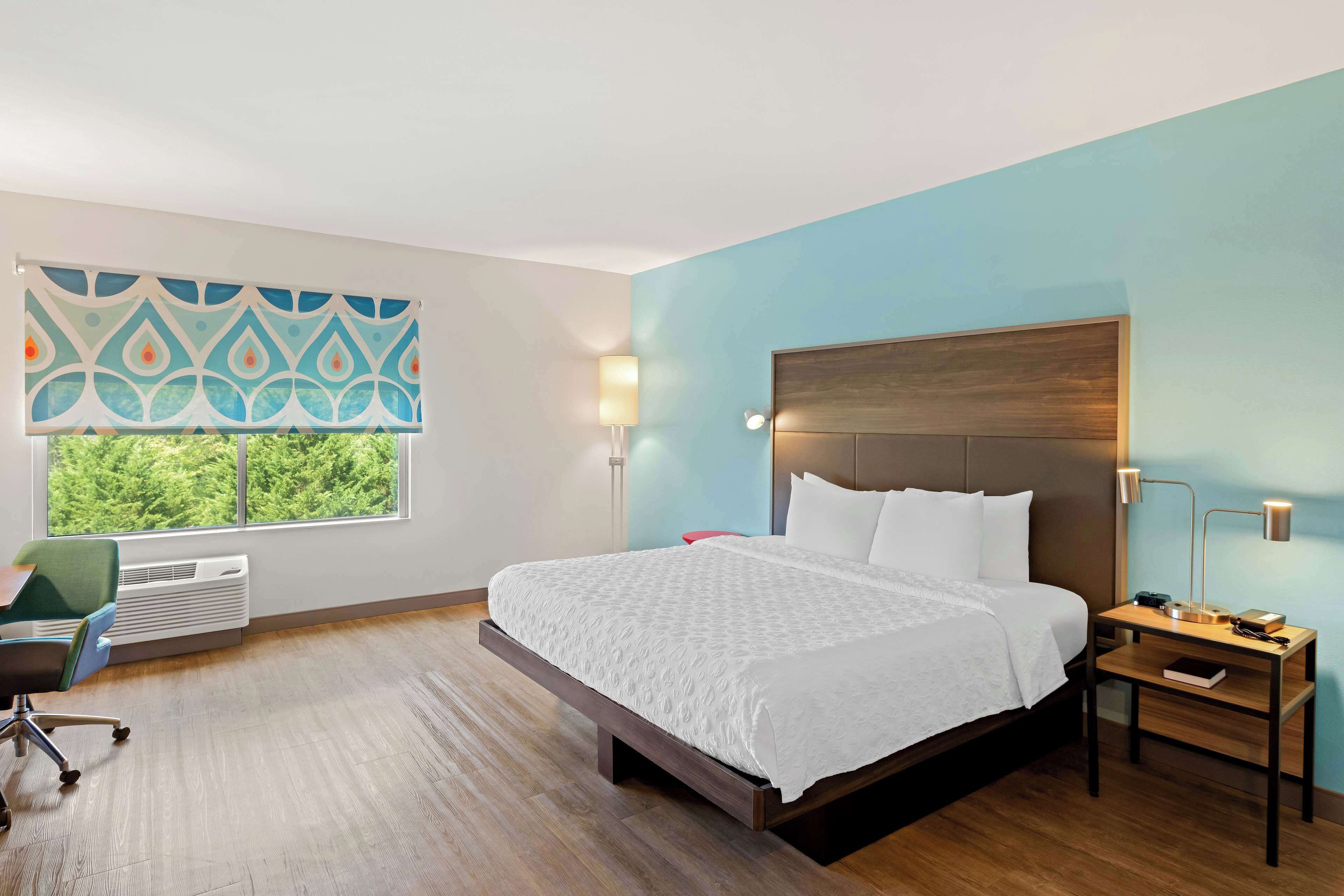 Hotelkamer met een groot bed, een bureau met lamp, een stoel en een raam met uitzicht op bomen.
