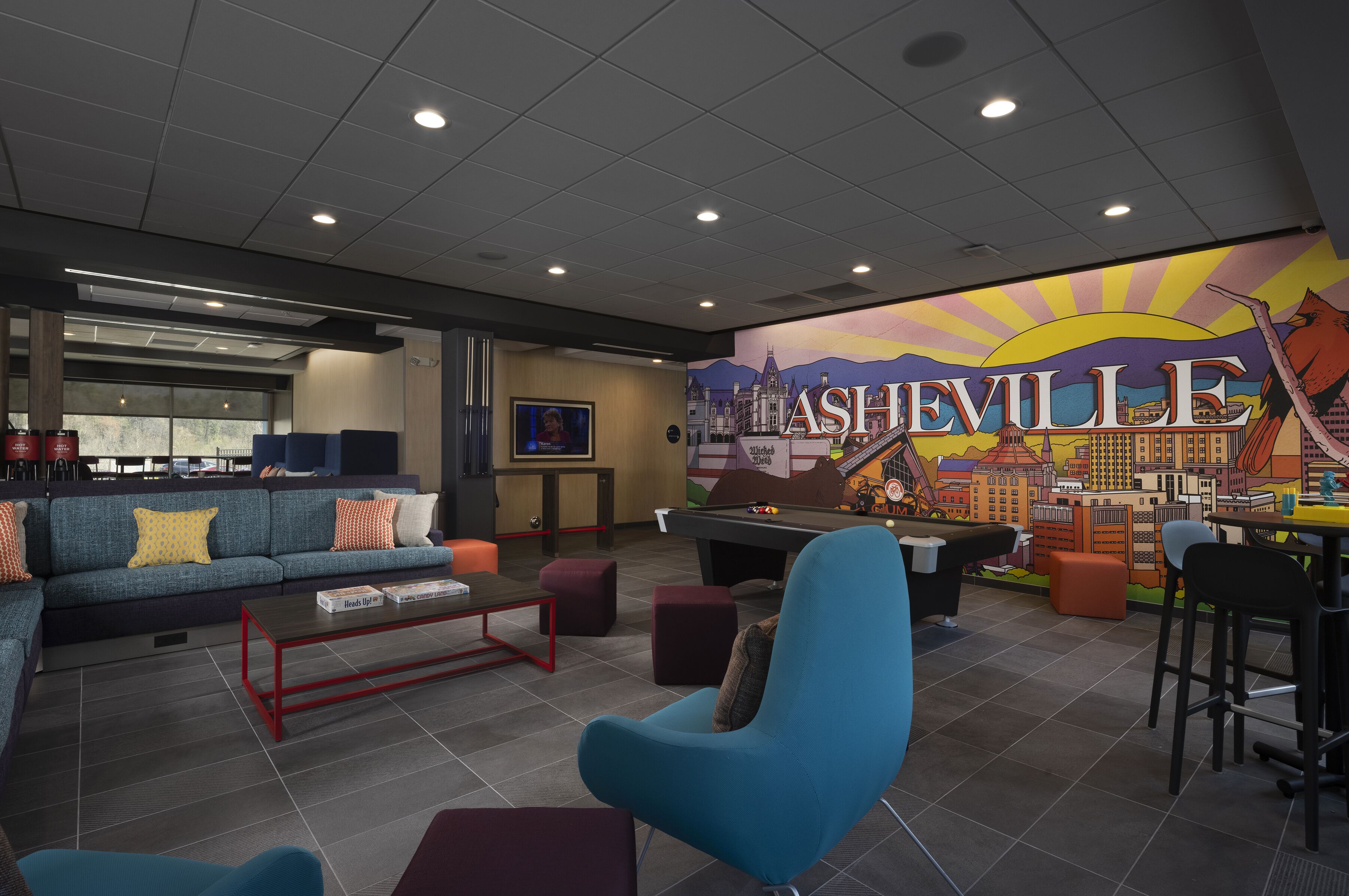 A pool table, blue chairs, a sofa, and a mural of Ashville.