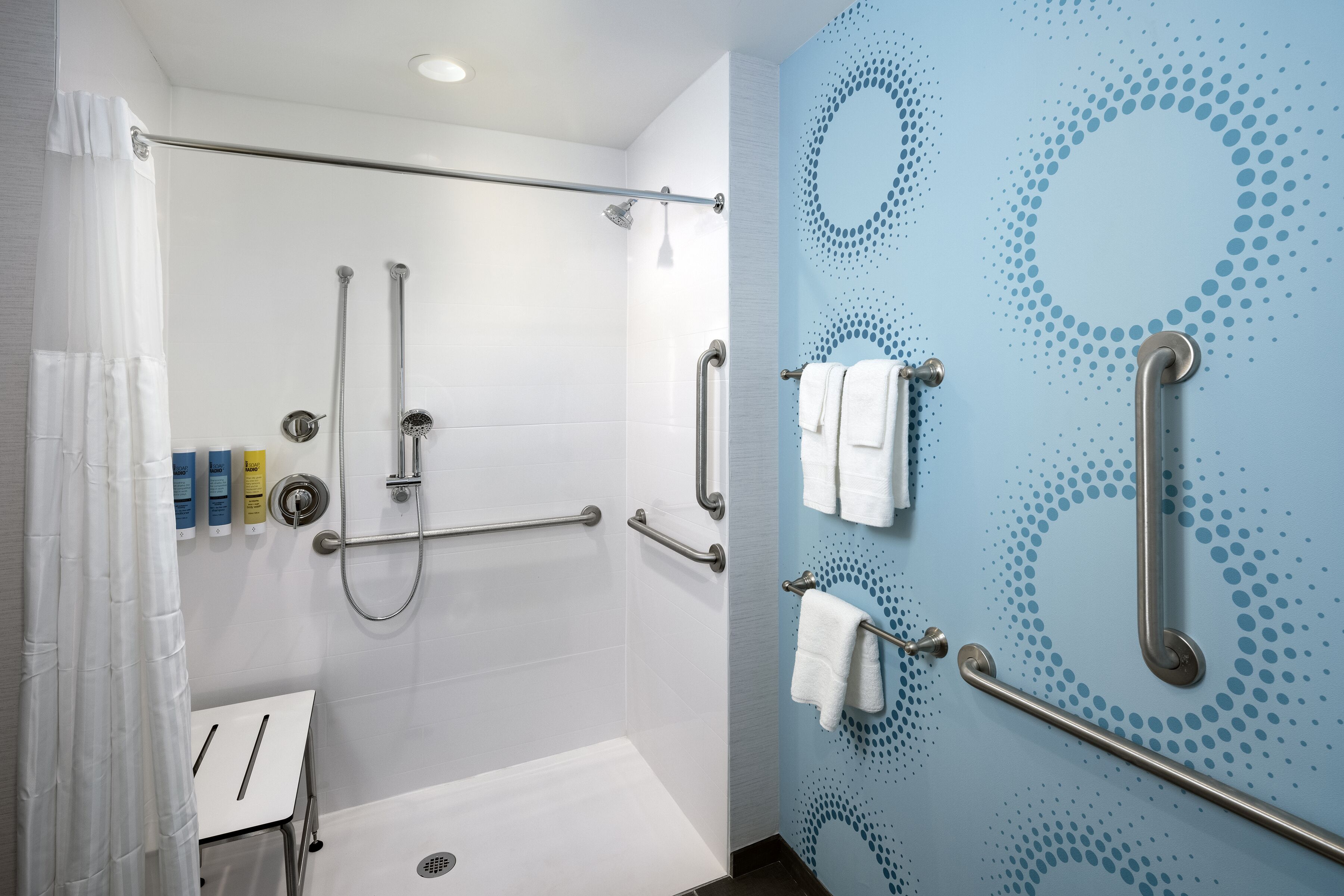 A modern bathroom with a shower, grab bars, and a towel rack.