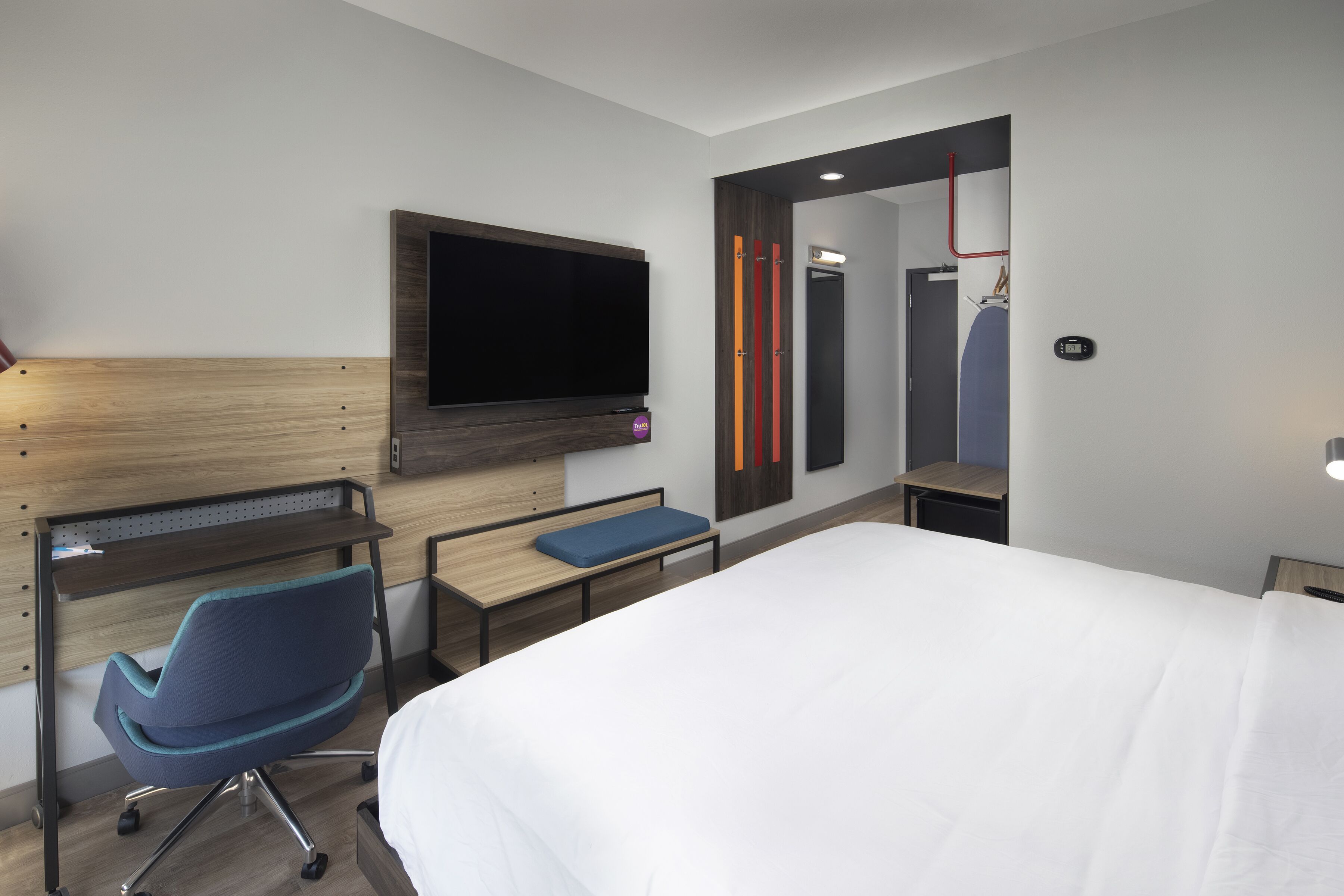 A modern hotel room with a large bed, a desk with a chair, a flat-screen TV, and a mirror.