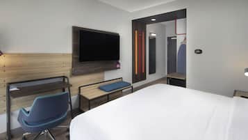 A modern hotel room with a large bed, a desk with a chair, a flat-screen TV, and a mirror.