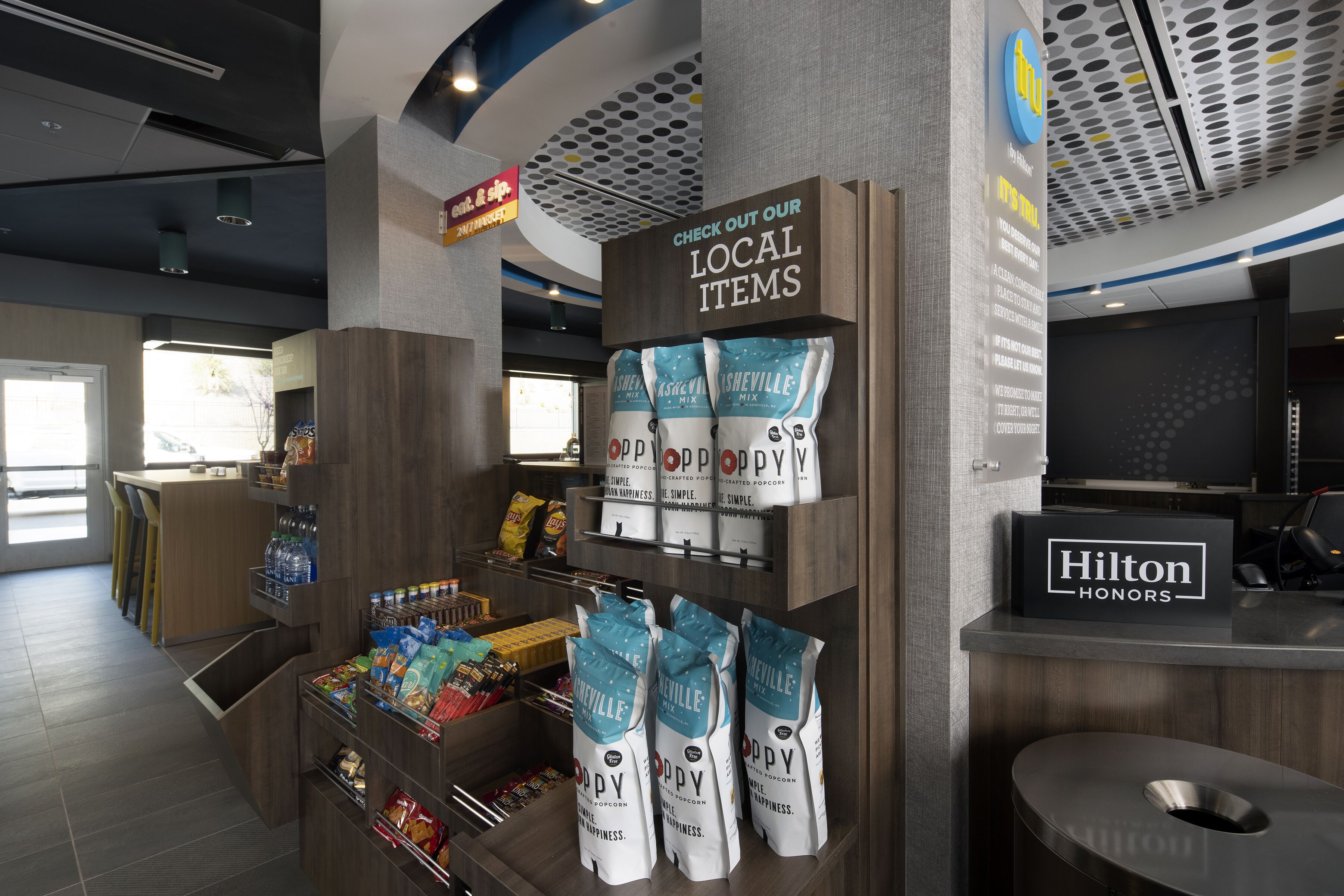 Eine Hotteleville mit einem 'Hilton Honors'-Schild, einer Produktpräsentation mit regionalen Artikeln und einer Auswahl an Snacks und Getränken.