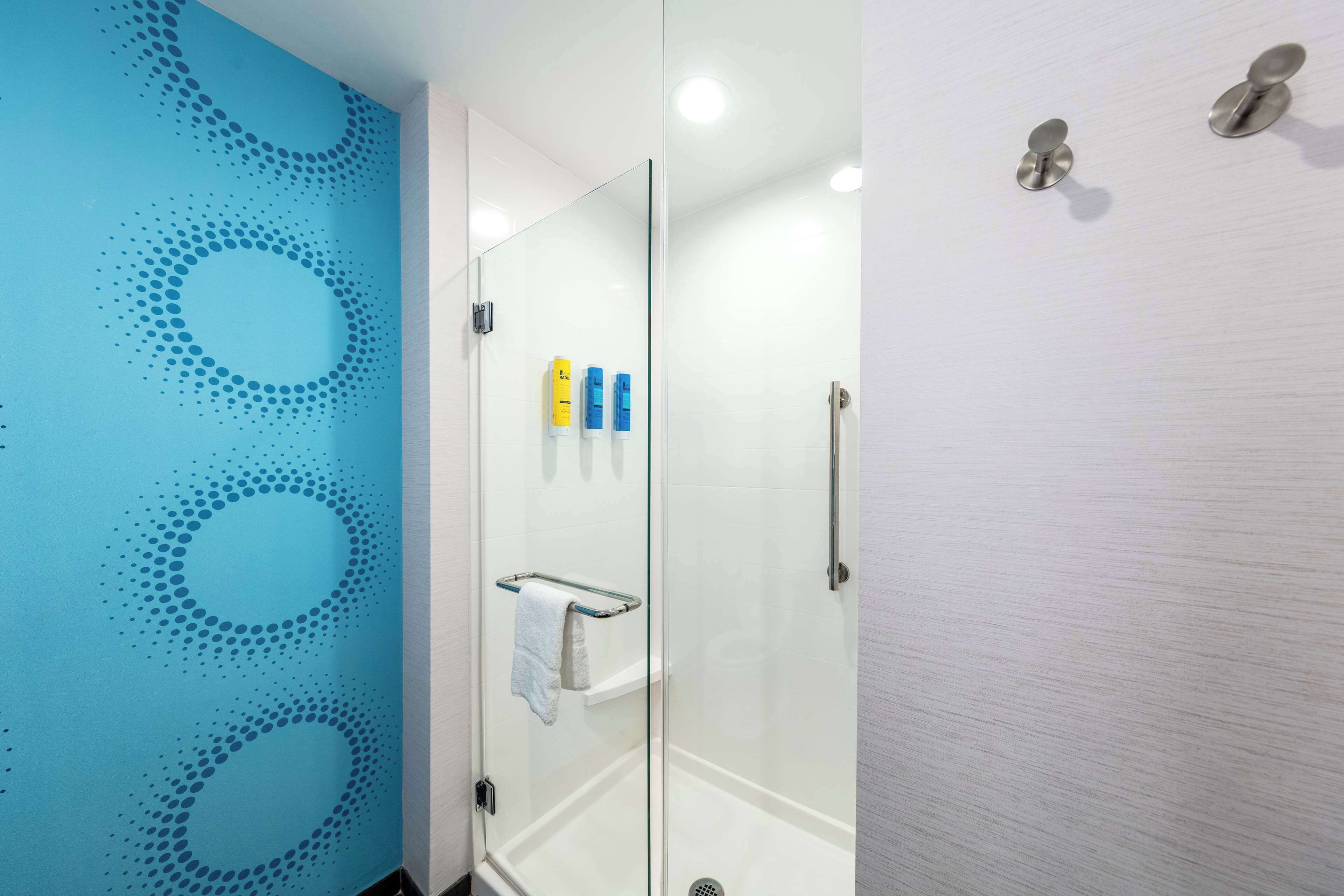 A modern bathroom with a glass shower enclosure, a towel rack, and toiletries on the wall.