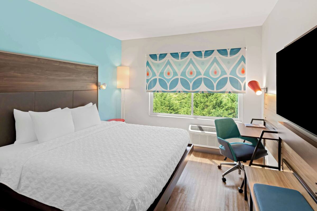 Ein Hotelzimmer mit einem großen Bett, einem Schreibtisch mit Stuhl, einem Fernseher und einem Fenster mit Blick auf Grünflächen.