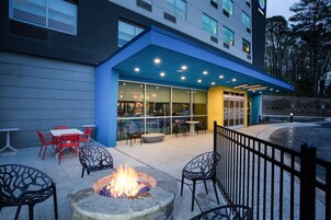 An outdoor patio with a fire pit, red and black chairs, and a glass-enclosed restaurant area.