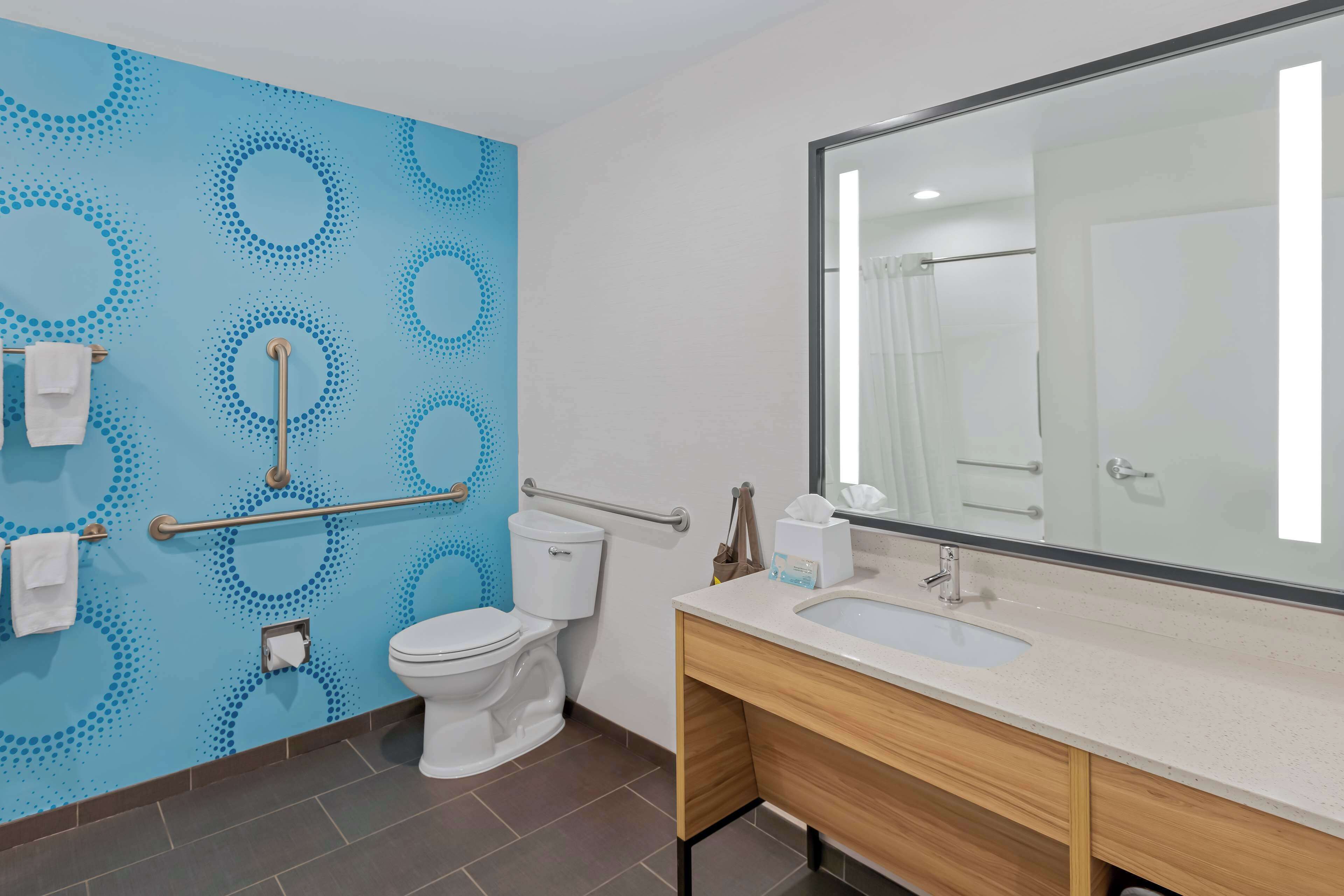 Un baño moderno con una pared azul estampada, un inodoro blanco, un lavamanos con espejo y una barandilla.