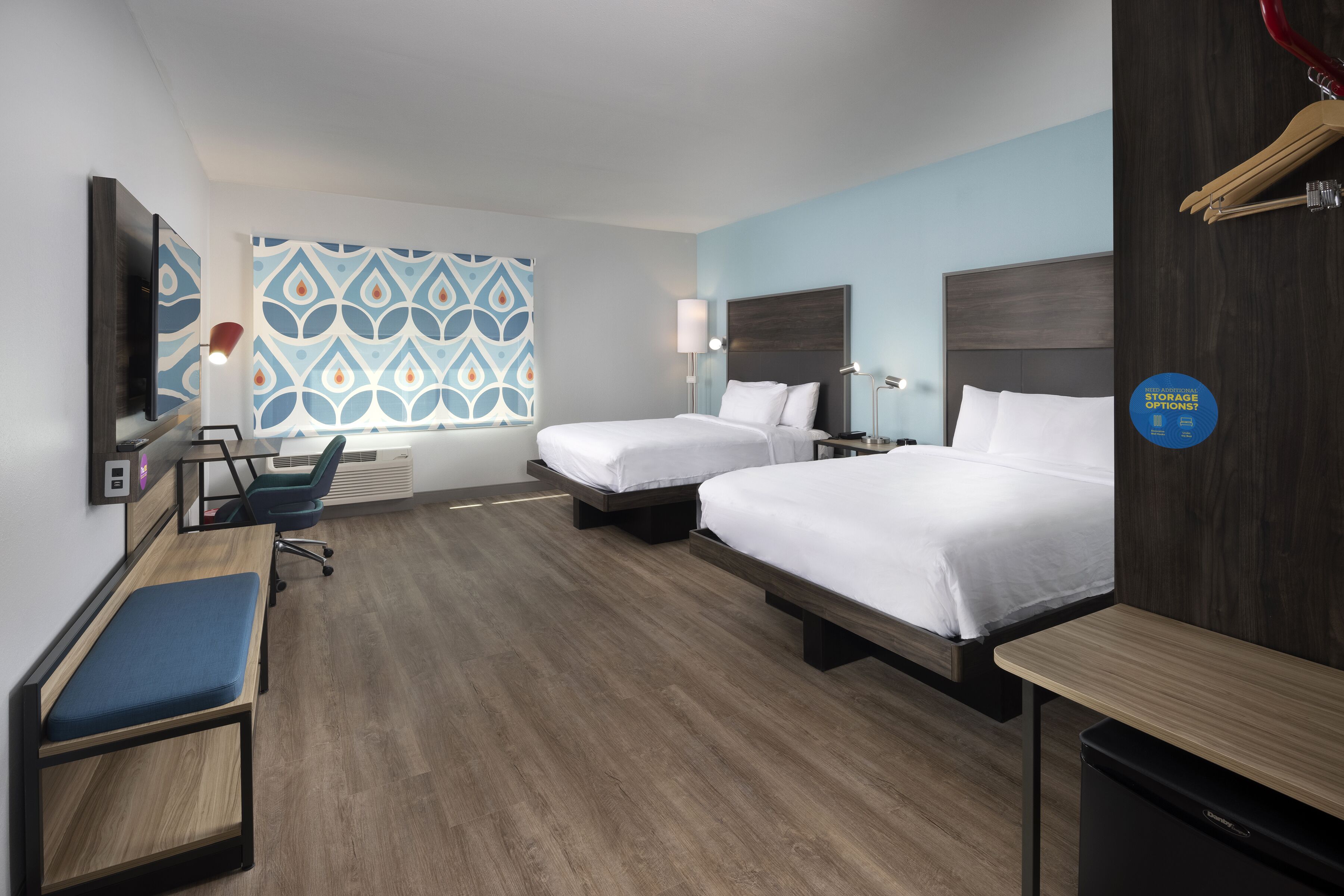 Ein Hotelzimmer mit zwei Betten, einem Schreibtisch, einem Stuhl, einem Fernseher und einer Wand mit Muster.