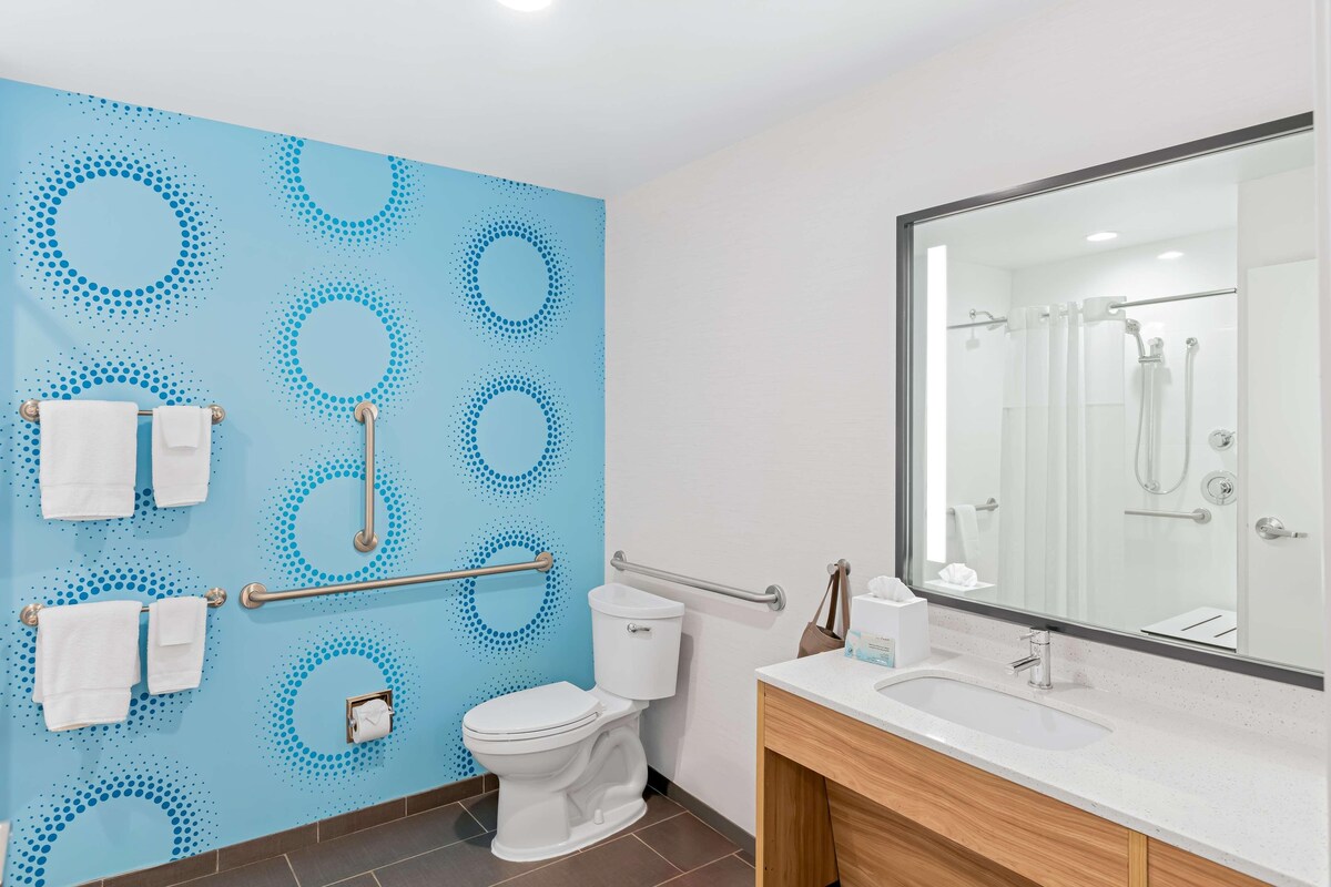 Ein modernes Badezimmer mit blauem Wandmuster, einer weißen Toilette, einem Waschbecken und einem großen Spiegel.
