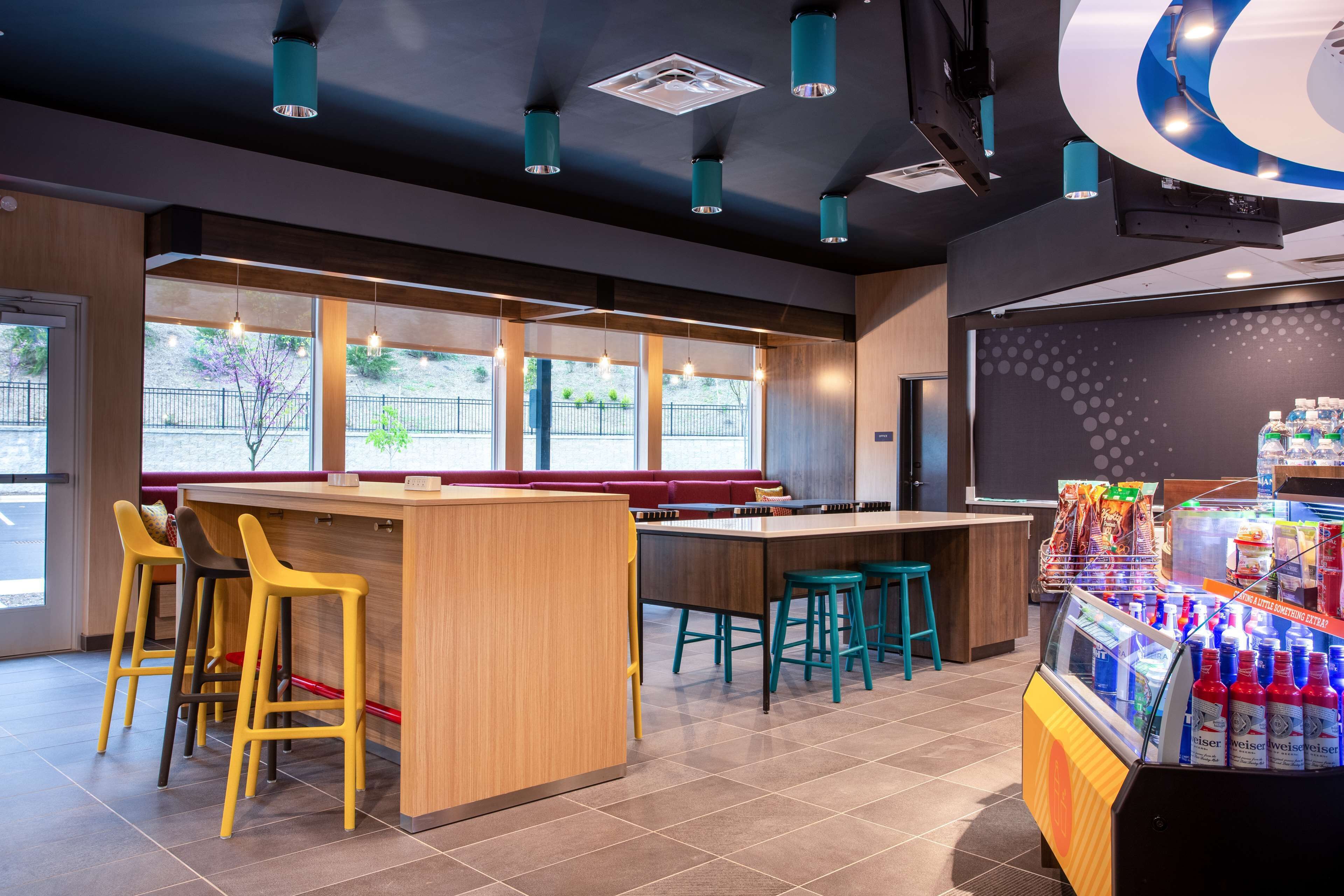 Zona de bar moderna con una barra de madera, taburetes amarillos y turquesa y un dispensador de bebidas.