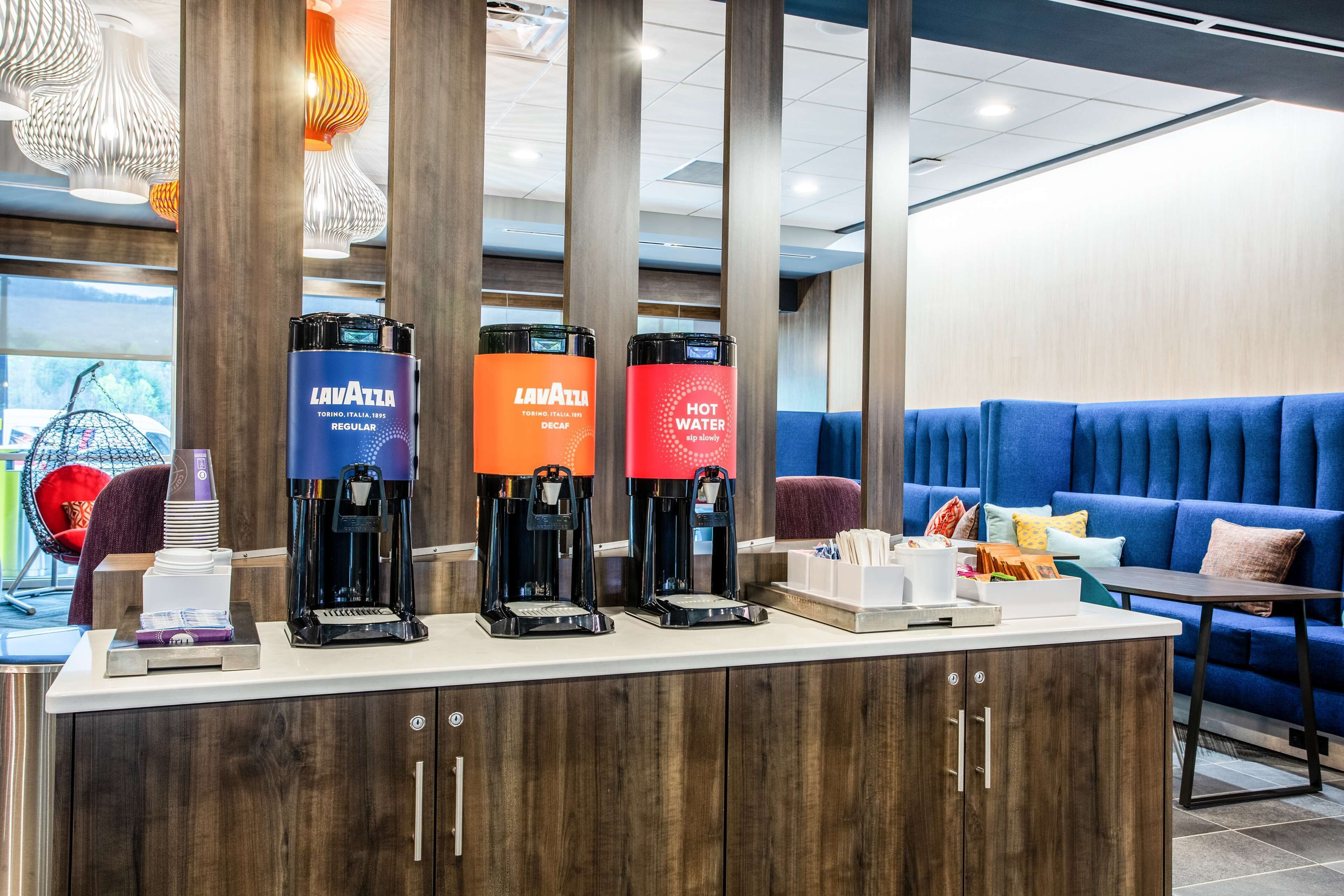 A coffee station with three coffee makers, a counter with a coffee machine, and a seating area with a blue couch and a small table.