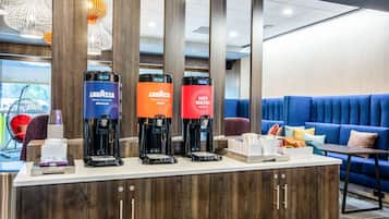 A coffee station with three coffee makers, a counter with a coffee machine, and a seating area with a blue couch and a small table.