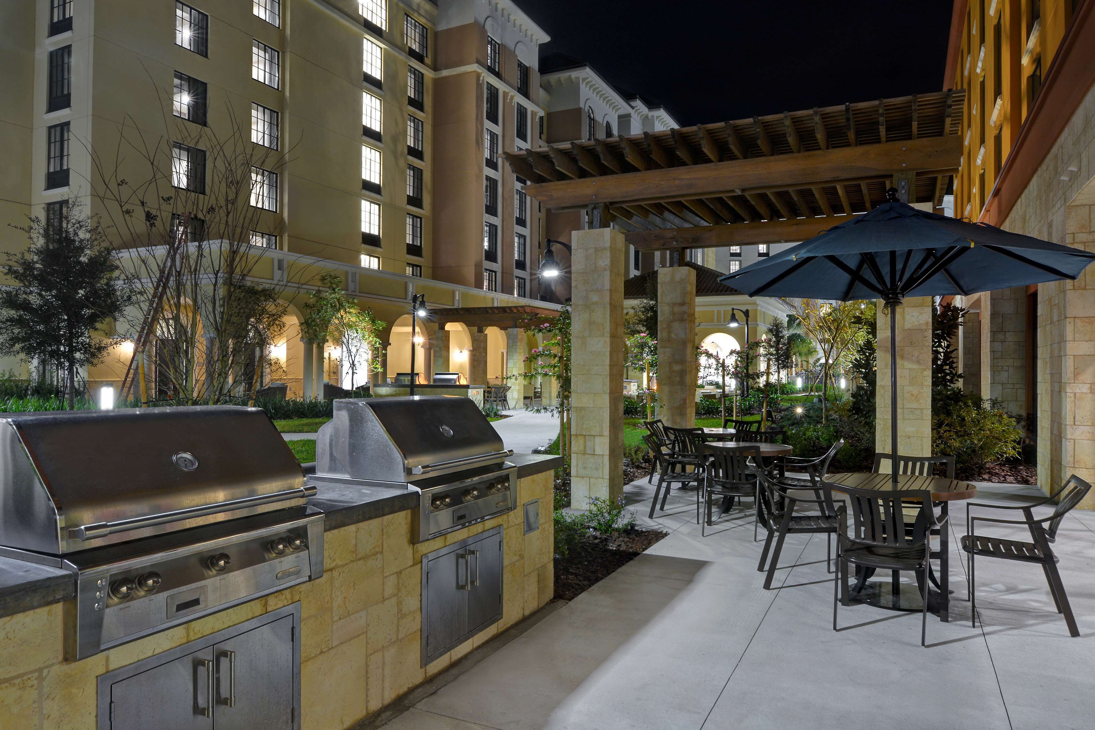 An outdoor patio area with a barbecue grill, dining tables, and chairs.