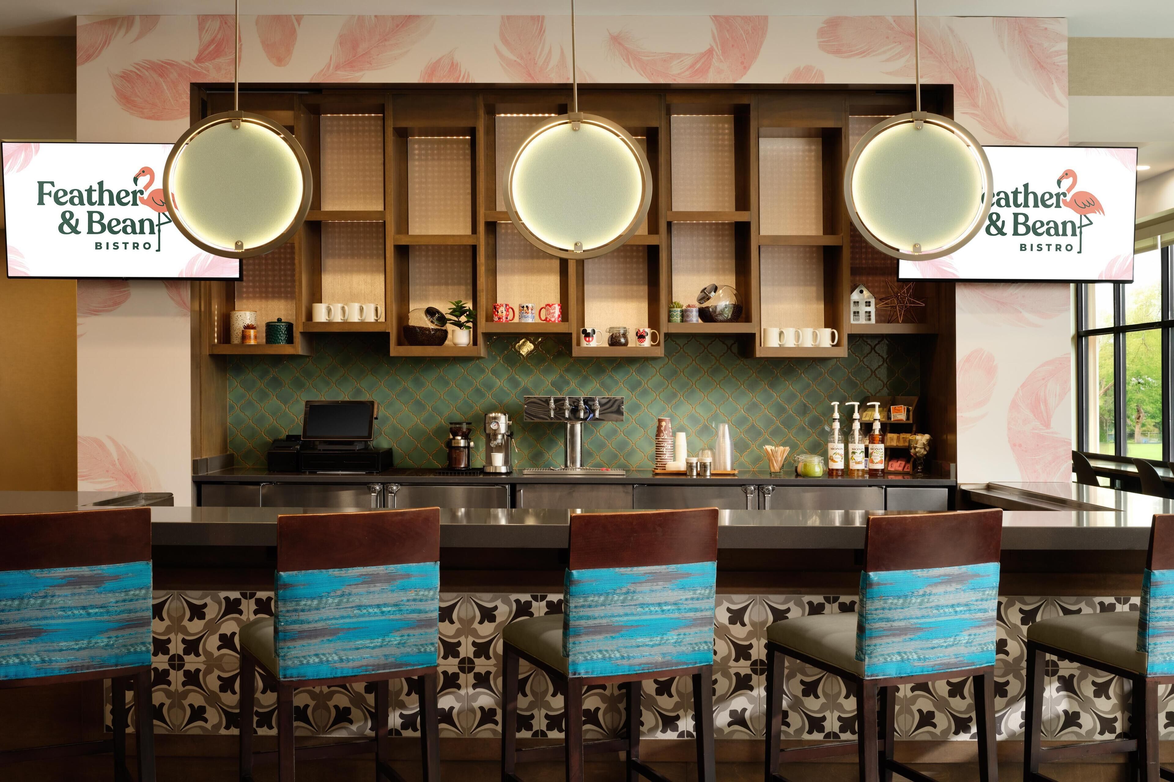 Zona de bar con un letrero que dice "Feather & Bean Bistro", taburetes con asientos azules y un salpicadero con diseño.