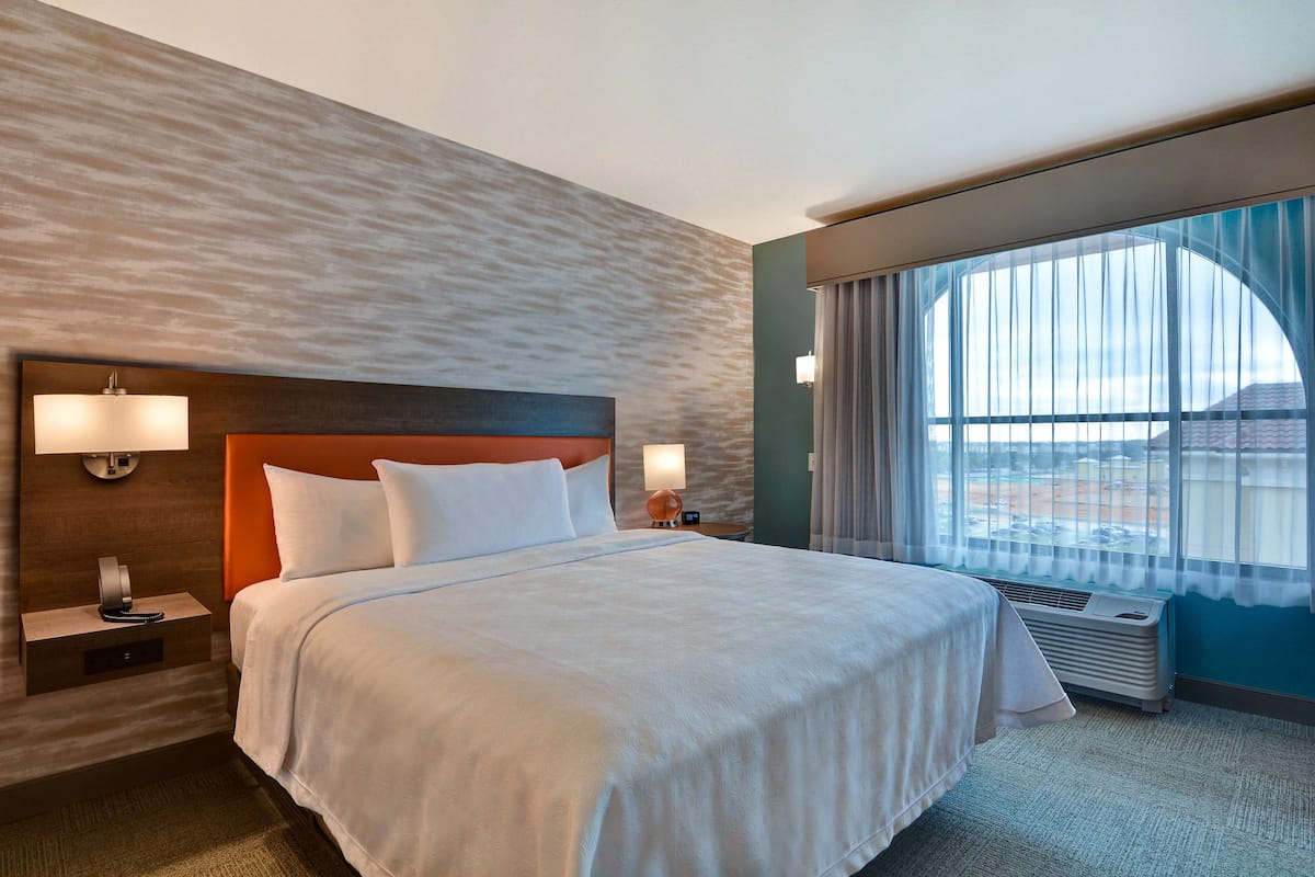 Una habitación de hotel con una cama grande, dos lámparas de noche, un calentador y una ventana con cortinas.