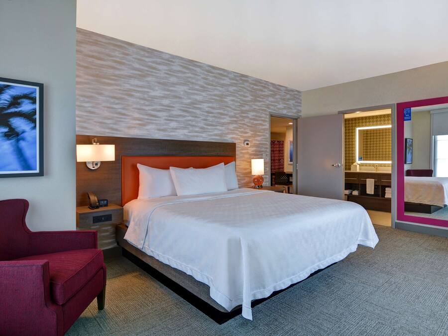 Ein Hotelzimmer mit einem großen Bett, einem roten Sessel, einem an der Wand montierten Fernseher und einem durch eine offene Tür einsehbaren Badezimmer.